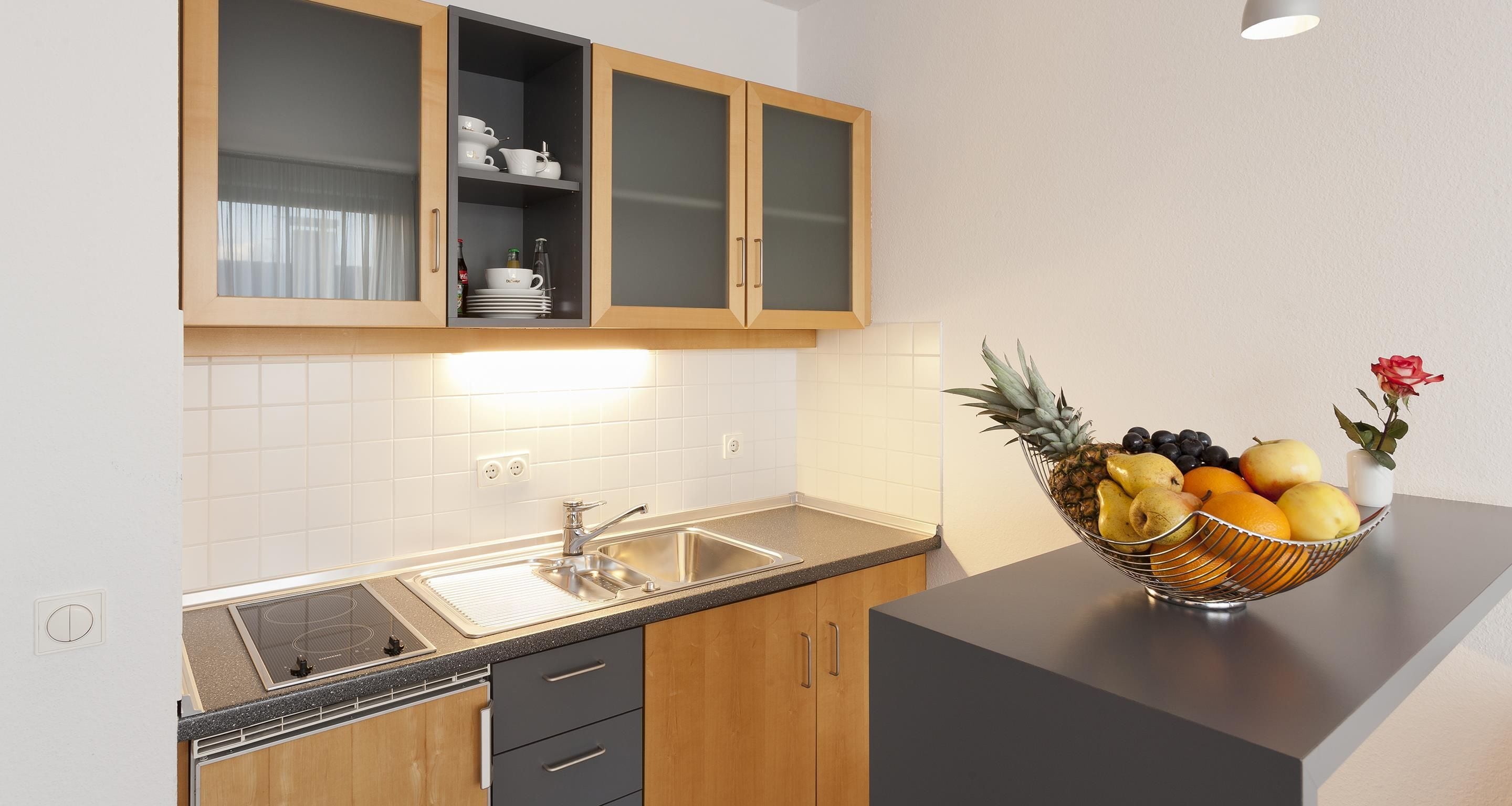 A kitchen with wooden cabinets, a stainless steel sink, and a fruit bowl on the counter.