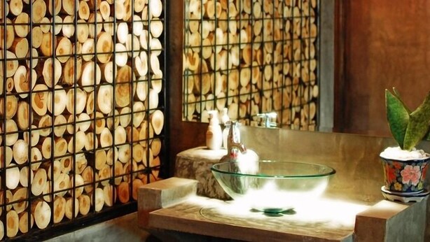 Ein Badezimmer mit einer Wand aus Holzstämmen, einem Glasklopfteil und einem Behälter mit Blumenmuster.