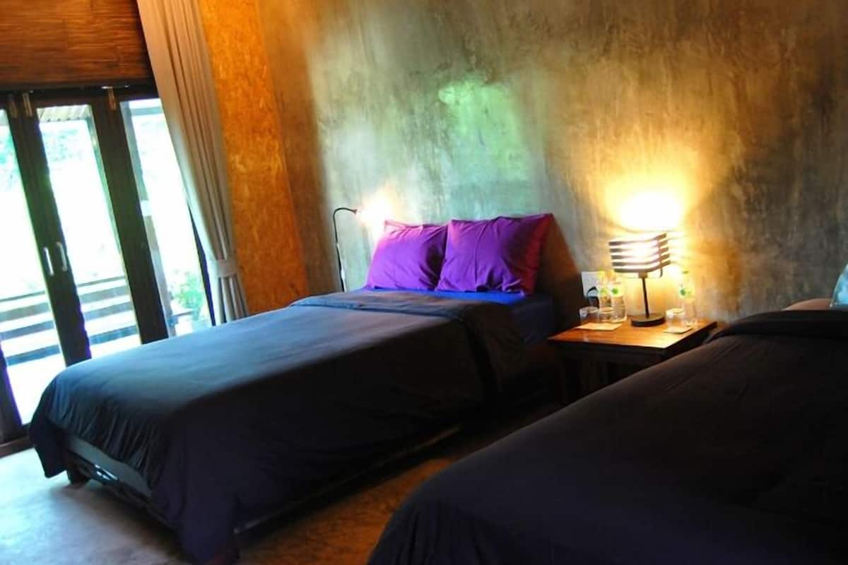 A room with two beds, a nightstand with a lamp, and a view of the outdoors through a glass door.