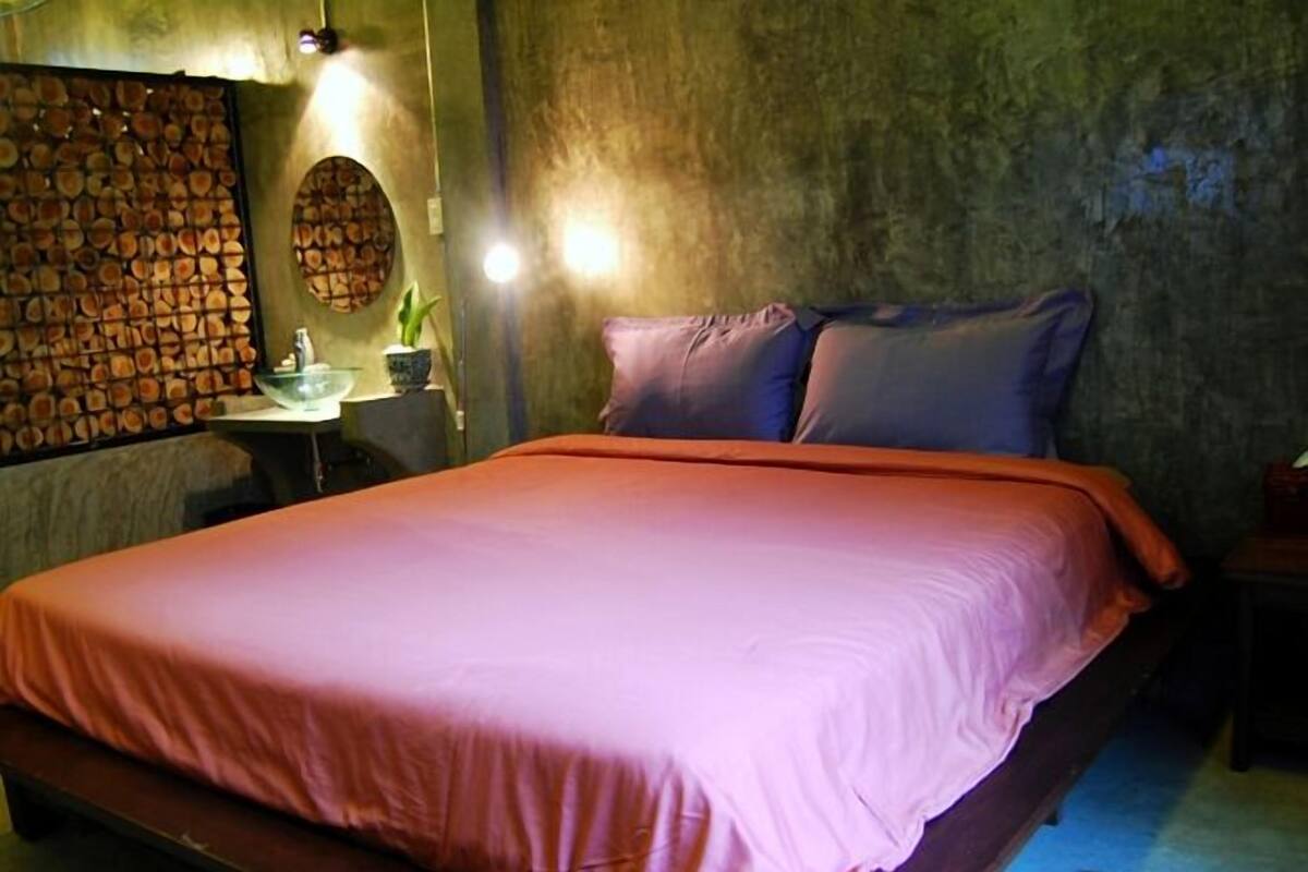A bedroom with a bed, a wall-mounted wooden panel, a round mirror, and a small table with a plant.