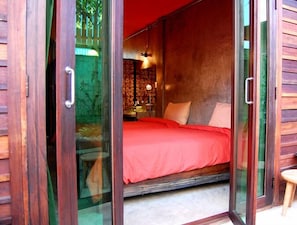 Camera da letto con copriletto rosso, testiera in legno e porta vetrata che dà su un balcone.