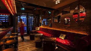 Eine Bar mit einer roten Ledersitzbank, Holzstühlen und Vintage-Koffern.
