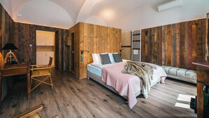 Ein Schlafzimmer mit Holzboden, einem Bett mit rosaroter Decke, einer Holzwand, einem kleinen Schreibtisch mit Lampe und einem Fenster.