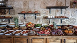 A buffet with various food items and a stone wall background. - Grand Cave Suites (Nevsehir)