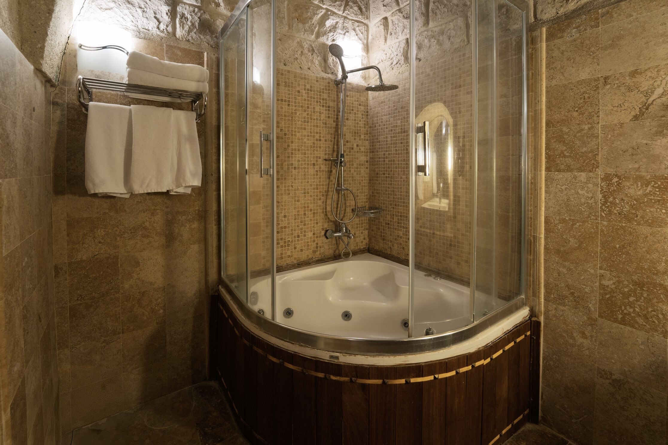 A walk-in shower with a glass enclosure, a wooden base, and a tiled wall.