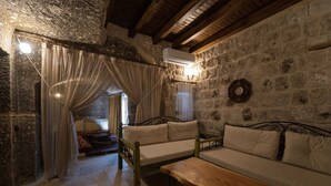 A rustic room with stone walls, a wooden bench, a sofa, and a bed with curtains. - Grand Cave Suites (Nevsehir)