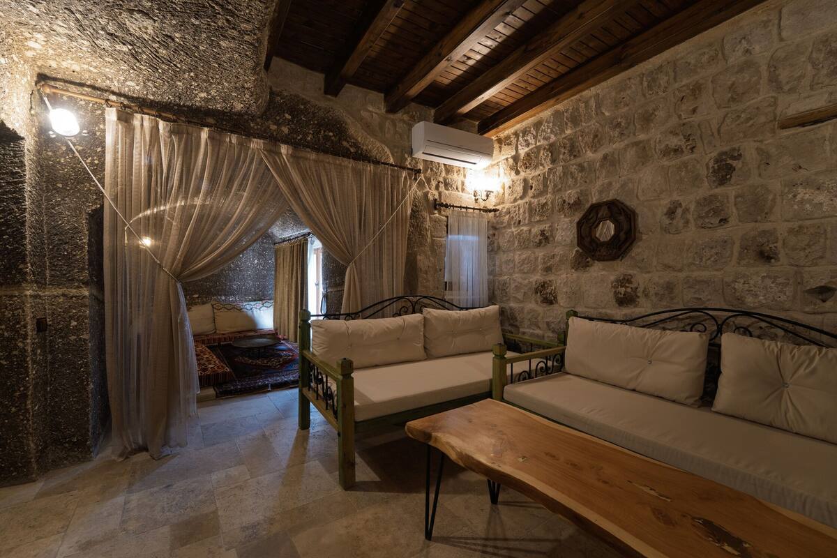 A rustic room with stone walls, a wooden bench, a sofa, and a bed with curtains.
