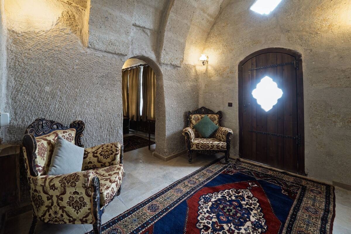 A room with a stone wall, a wooden door with a geometric glass window, a patterned sofa, and a large rug.