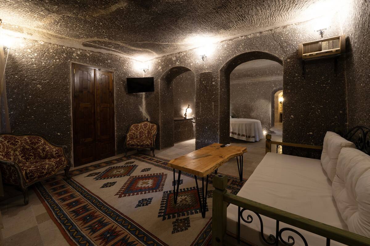 A room with a bed, a wooden table, a patterned rug, a sofa, and a TV mounted on the wall.