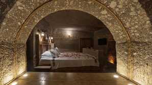 A bedroom with a stone archway, a bed with a floral bedspread, and a nightstand with a lamp. - Grand Cave Suites (Nevsehir)