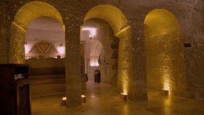 A dimly lit interior with stone arches and a central illuminated area, suggesting a historical or traditional setting. - Grand Cave Suites (Nevsehir)