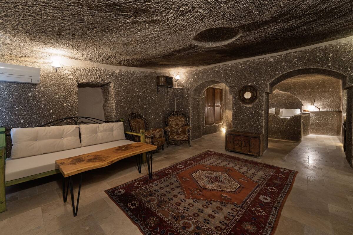 A room with a stone ceiling, a sofa, a wooden table, and a patterned rug.