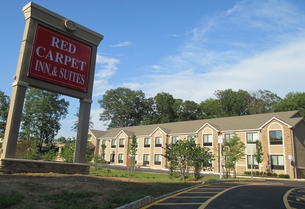 Edificio de Red Carpet Inn & Suites con un cartel, múltiples ventanas y un estacionamiento.