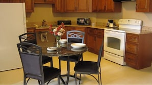 A kitchen with wooden cabinets, a dining table with chairs, a refrigerator, a microwave, a coffee maker, and an oven.