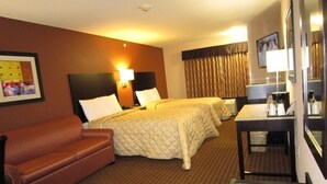 A hotel room with two beds, a sofa, a desk with a coffee maker, and a TV.