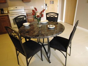 A round dining table with four black chairs, a vase with flowers, and plates and cutlery on the table.