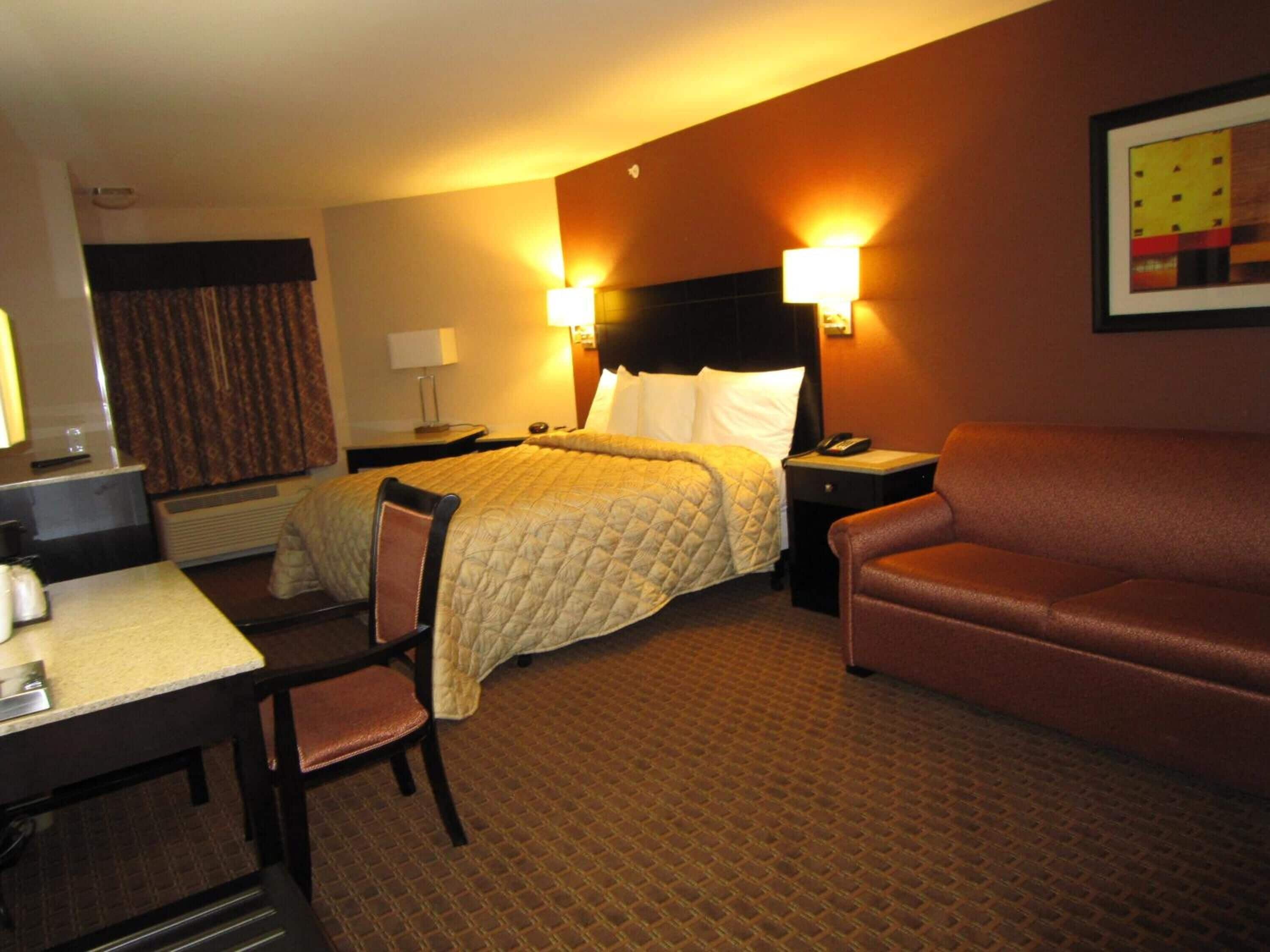 Una habitación de hotel con cama, escritorio, sillón, sofá y lámpara de pared.
