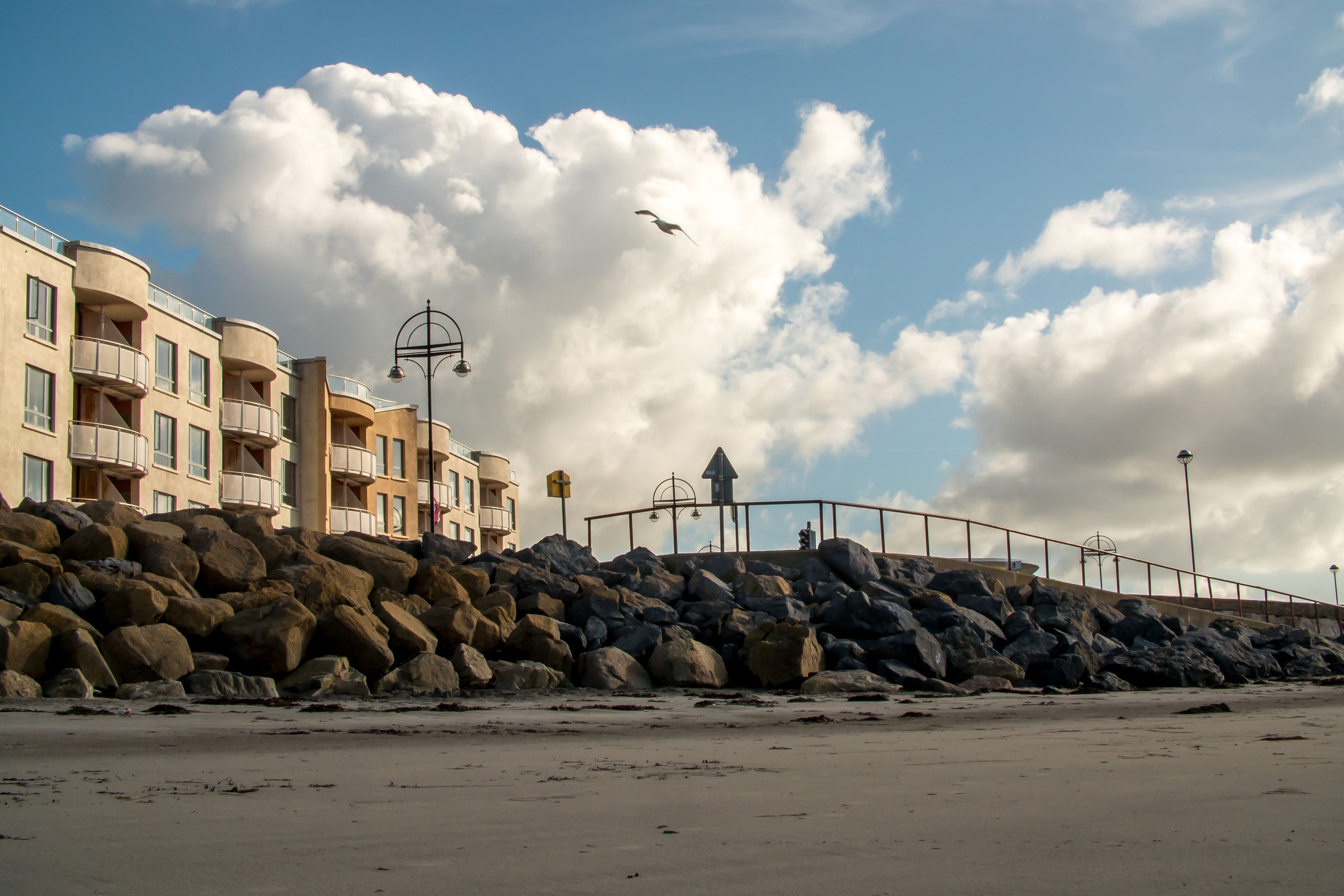 A beachfront hotel with multiple balconies, a rocky shoreline, and a clear sky.