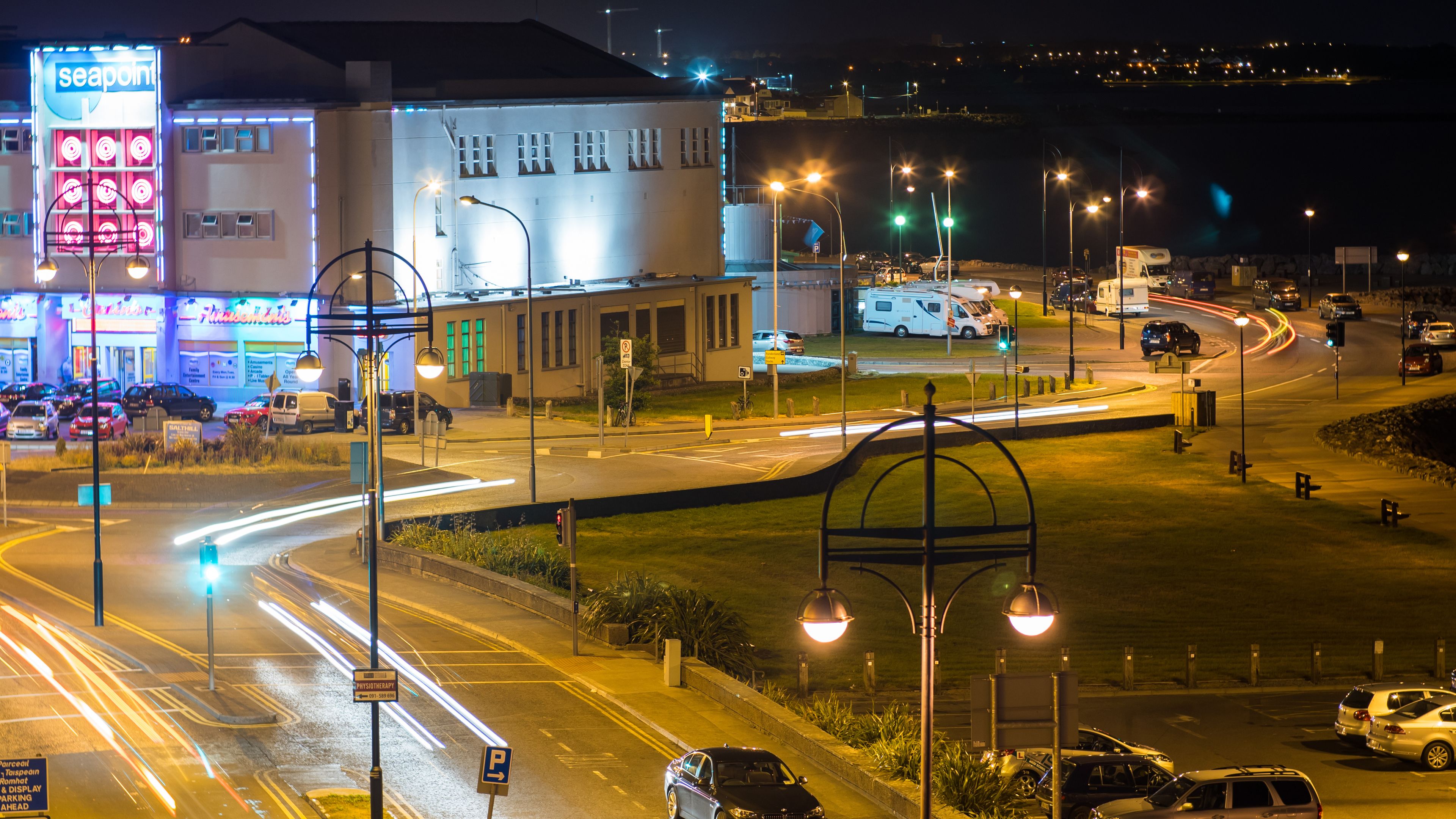 A nighttime urban intersection with traffic lights, street lamps, and a building with illuminated signage.