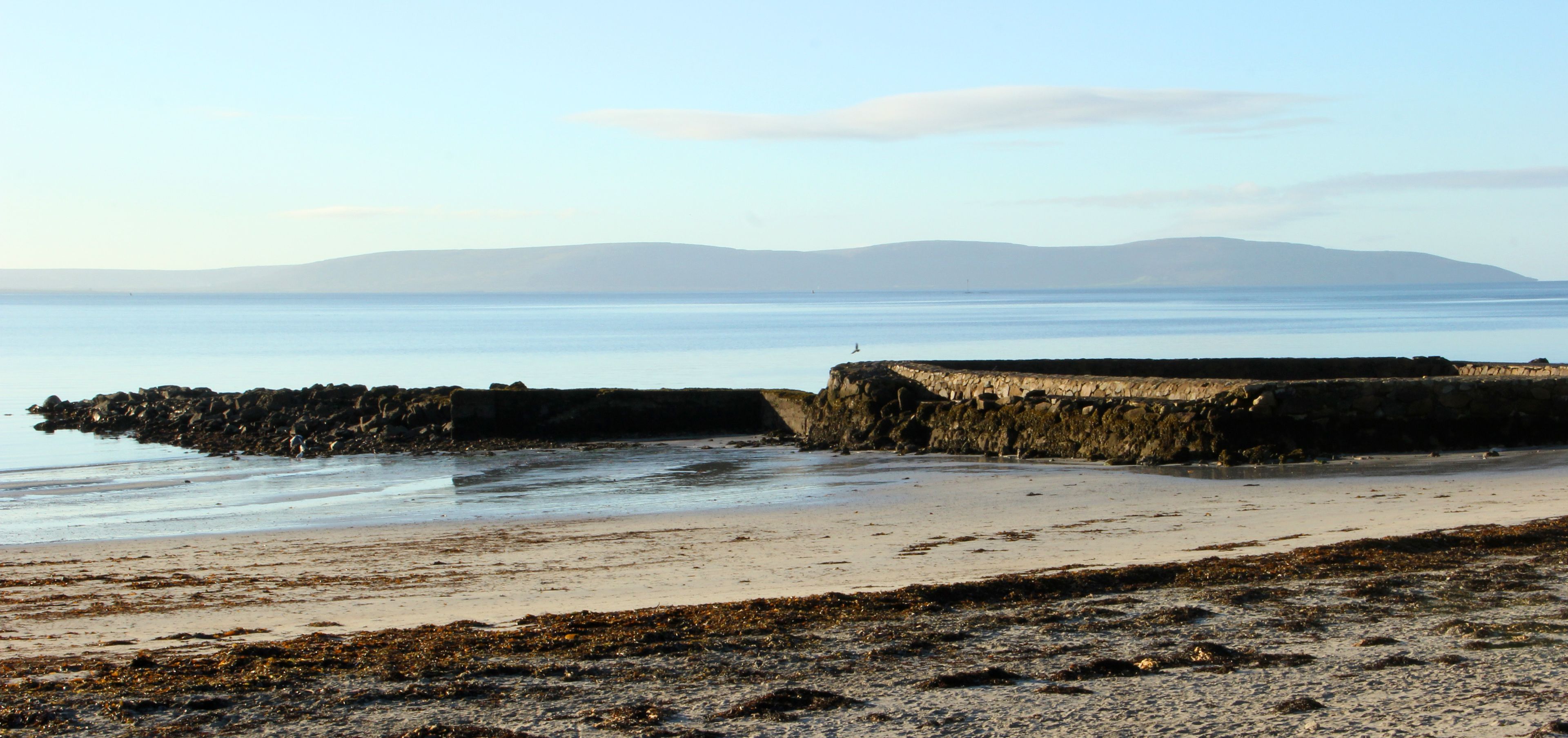 A coastal beach with a rocky breakwater and calm sea.