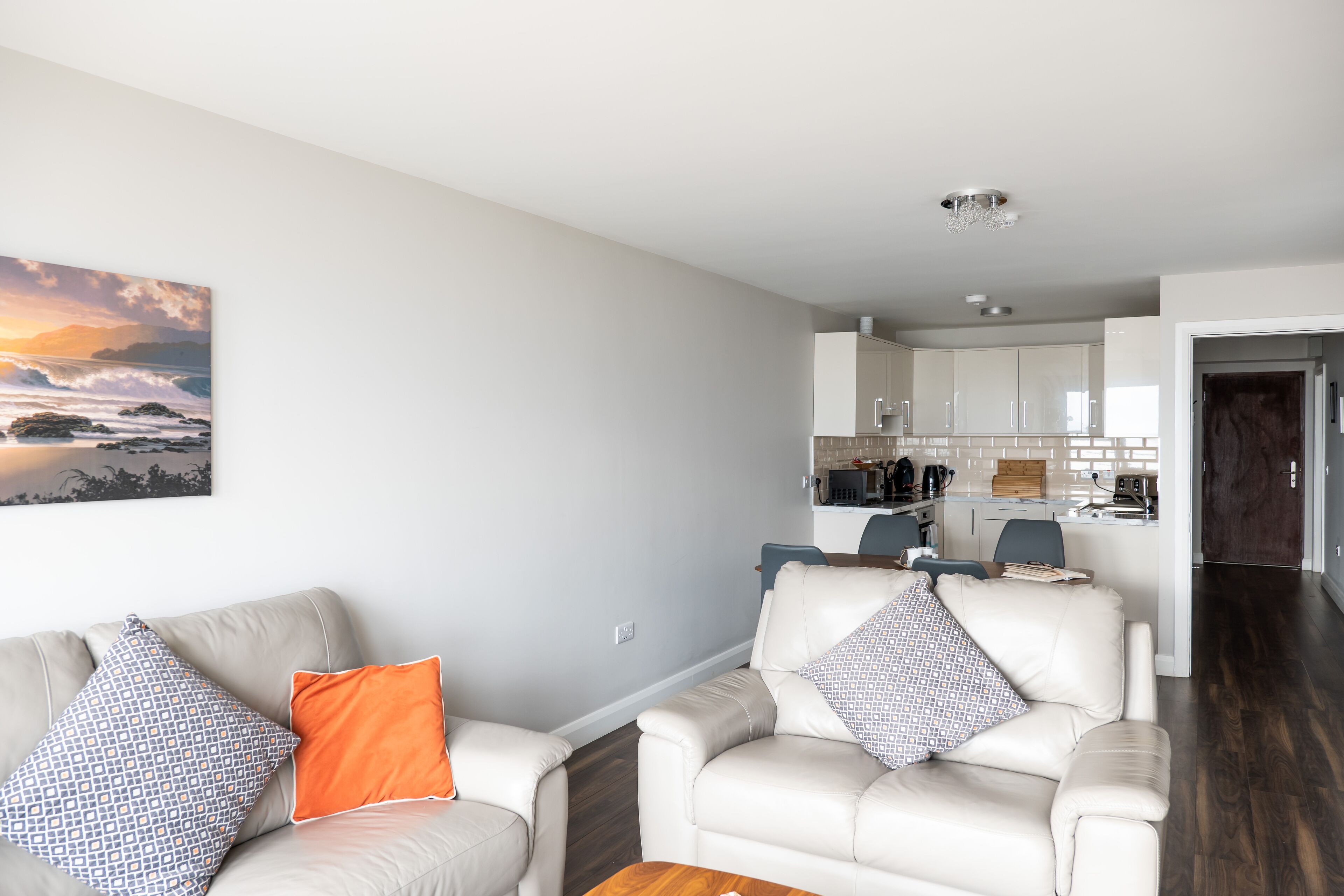 A modern living room with a sofa and armchairs, a wooden coffee table, and a kitchen in the background.