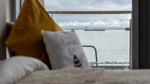 Ein Bett mit Kissen und Blick auf ein Schiff auf dem Wasser durch ein Fenster.