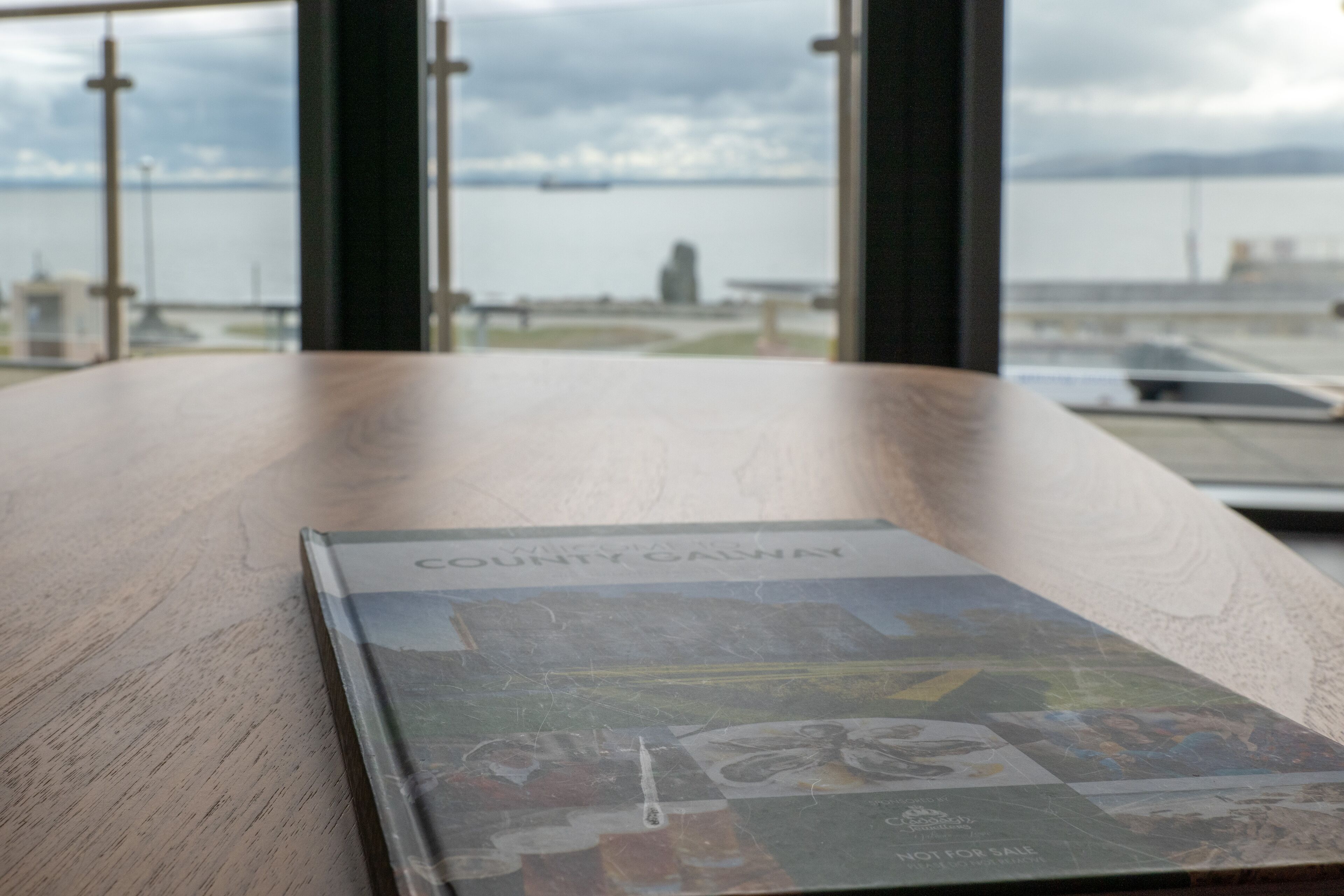 A wooden table with a book titled "COUNTY CAESNAY" and a view of a body of water through large windows.