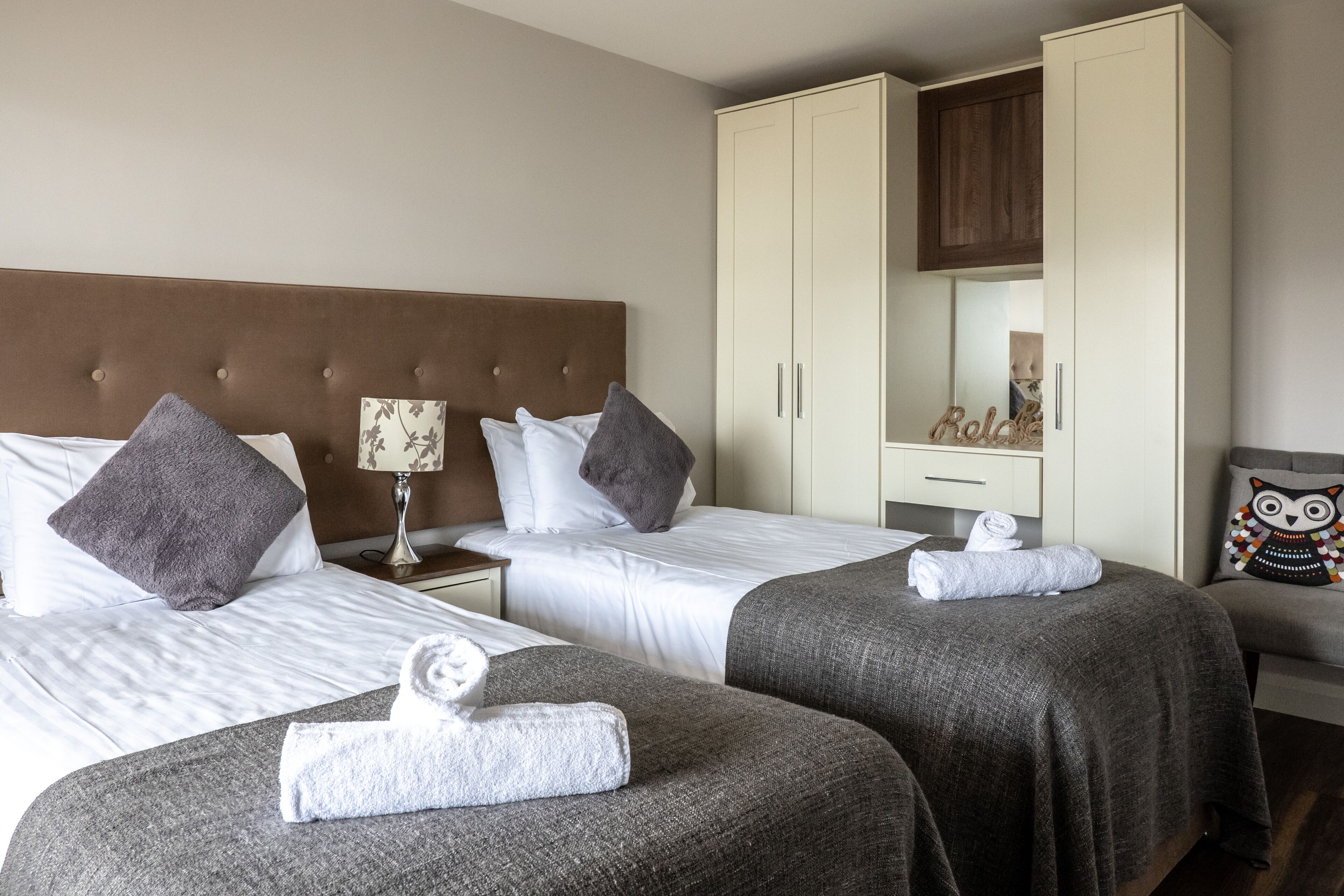 A hotel room with two beds, a wardrobe, a nightstand, and a mirror.