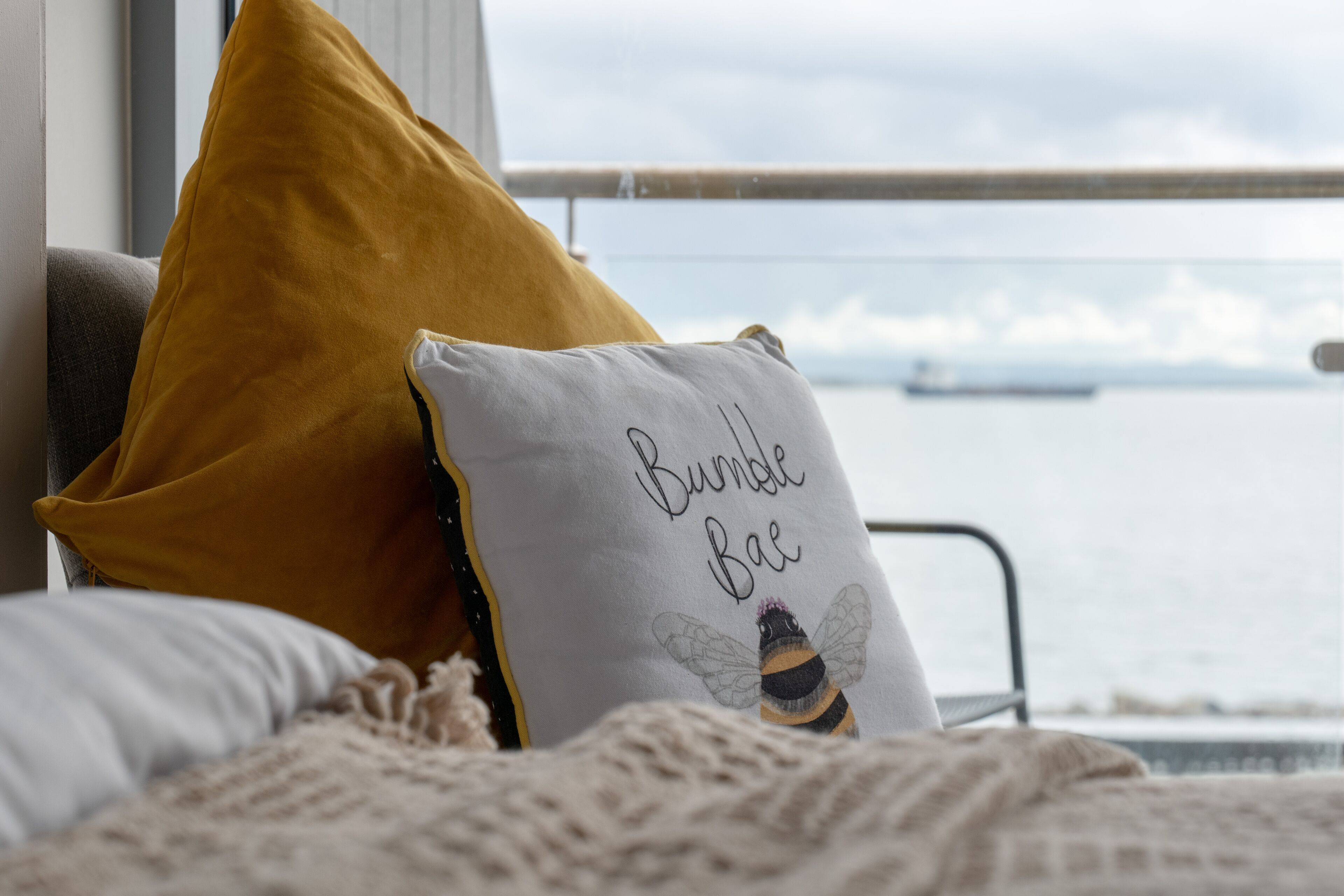 Una cama con un cojín color mostaza y un cojín blanco con un diseño de abeja y el texto 'Bumble Bae'.
