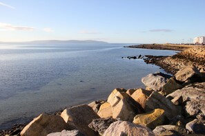 A coastal view with large rocks in the foreground and a distant shoreline with buildings. - Galway Bay Sea View Apartments (Galway)