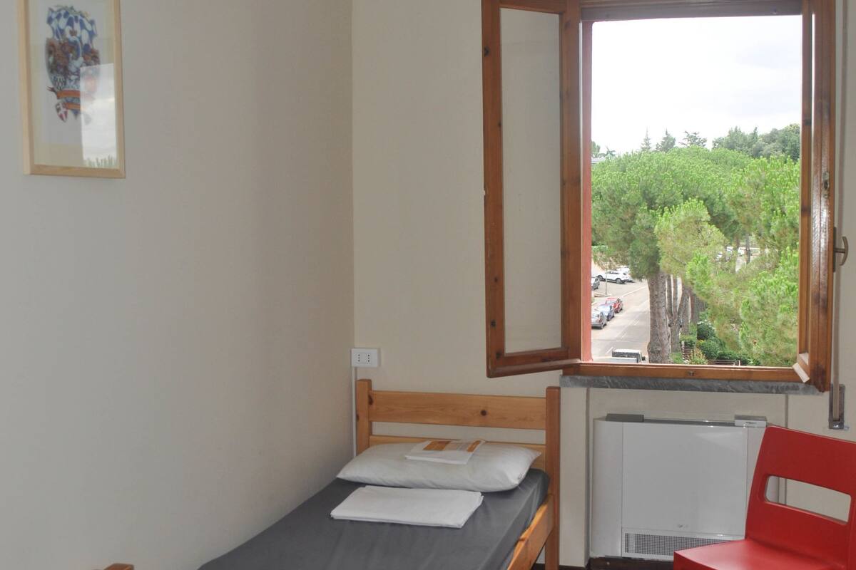 A small room with a bed, a chair, a window, and a radiator.