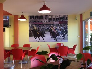 Un restaurante con sillas rojas, un gran mural de jinetes a caballo y un televisor montado en la pared.