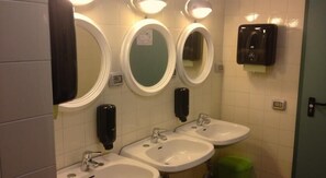 Baño con tres lavamanos, dos dispensadores de jabón y tres espejos iluminados.