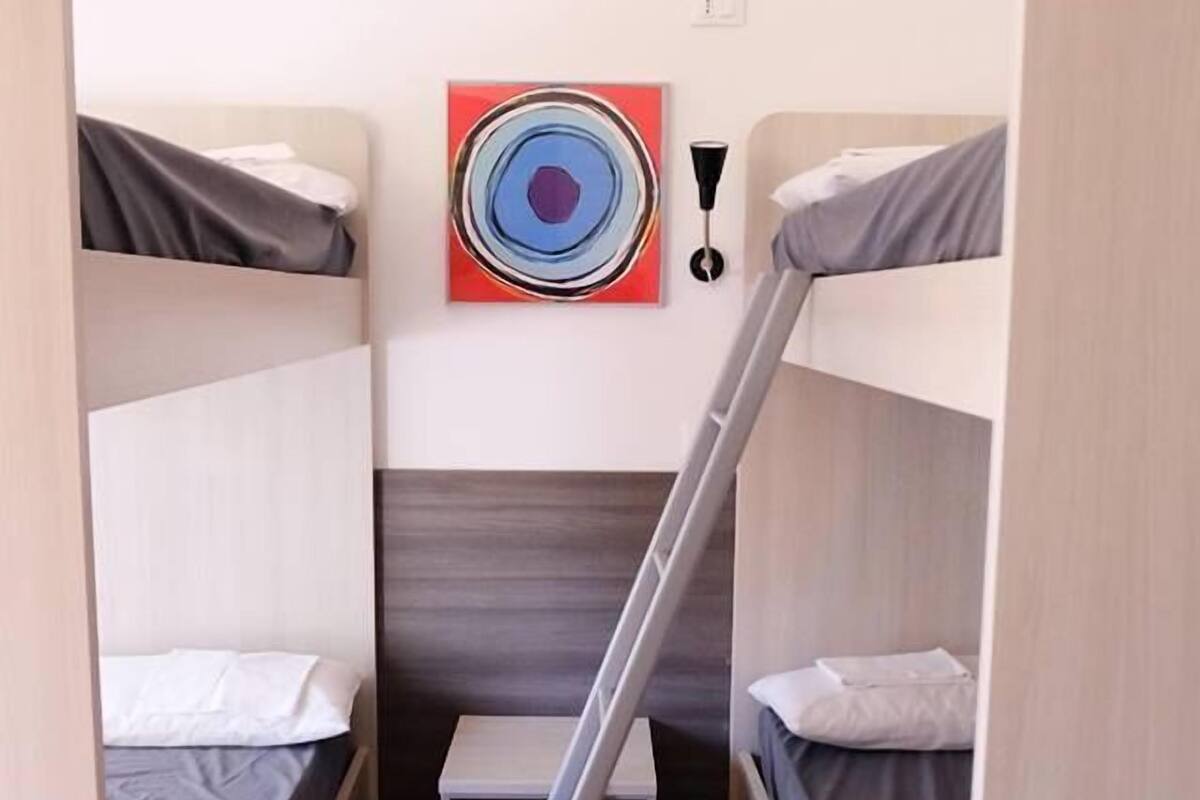 A compact room with bunk beds, a ladder, a small table, and a colorful painting on the wall.