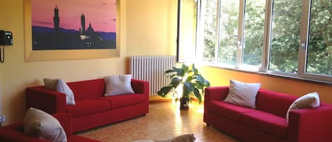 Una sala de estar con dos sofás rojos, un ventanal con vistas a árboles y un radiador.