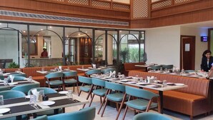 A restaurant with booths and tables, large windows, and a view of the outdoors. - juSTa Riverside Resort - Srinagar (Devaprayag)