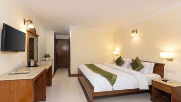 Quarto de hotel com cama, mesas de cabeceira, escrivaninha, televisão e porta que dá para outro cômodo.