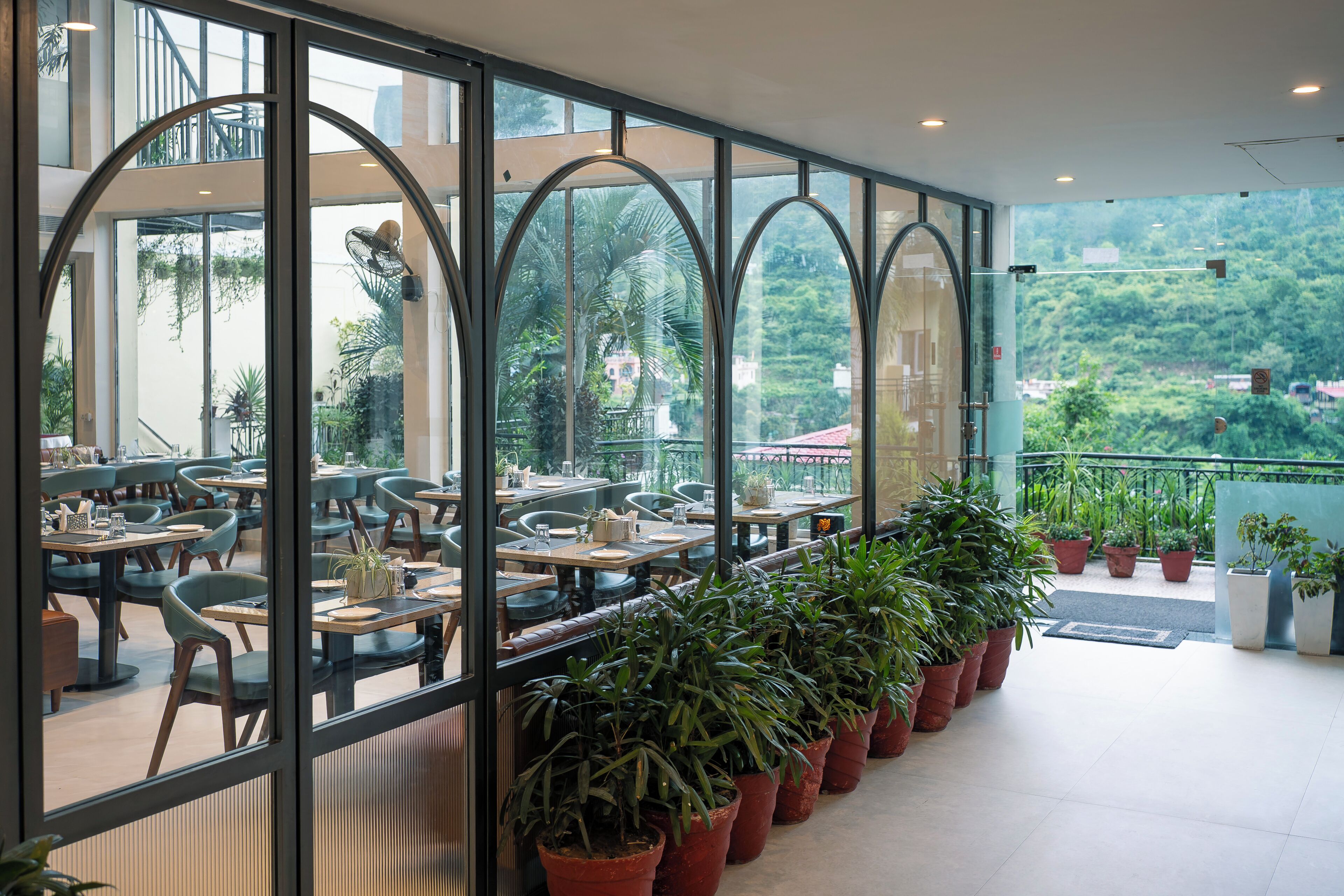 Um restaurante com área externa, grandes janelas e plantas em vasos.