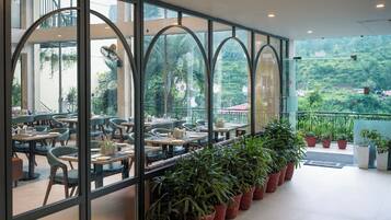 Um restaurante com área externa, grandes janelas e plantas em vasos.