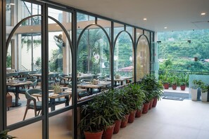 A restaurant with outdoor seating, large windows, and potted plants.