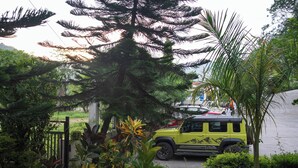 A yellow SUV parked in a lush garden with various plants and a tall tree. - juSTa Riverside Resort - Srinagar (Devaprayag)