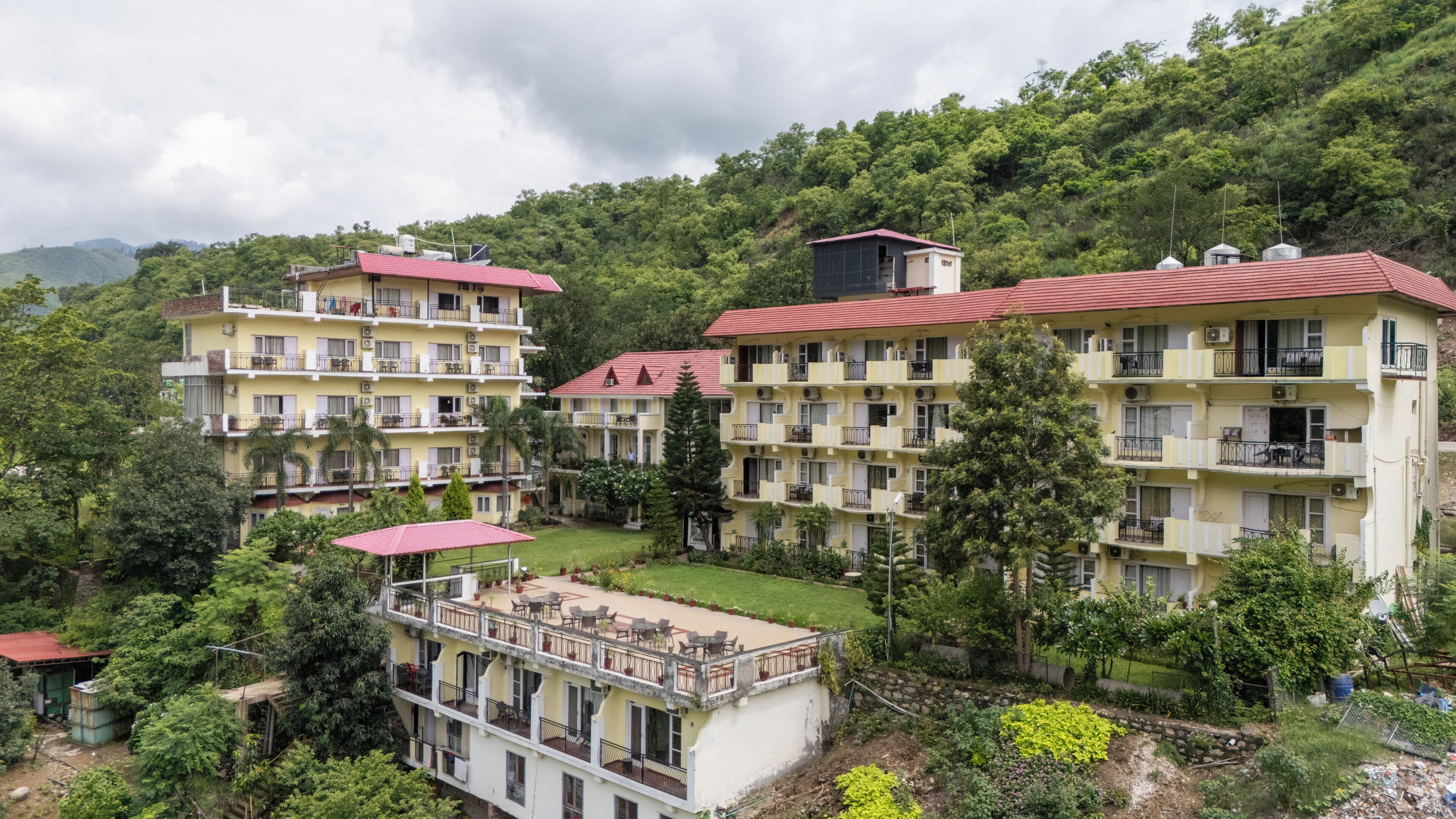 A multi-story hotel with balconies, a rooftop terrace, and lush greenery surrounding the property.