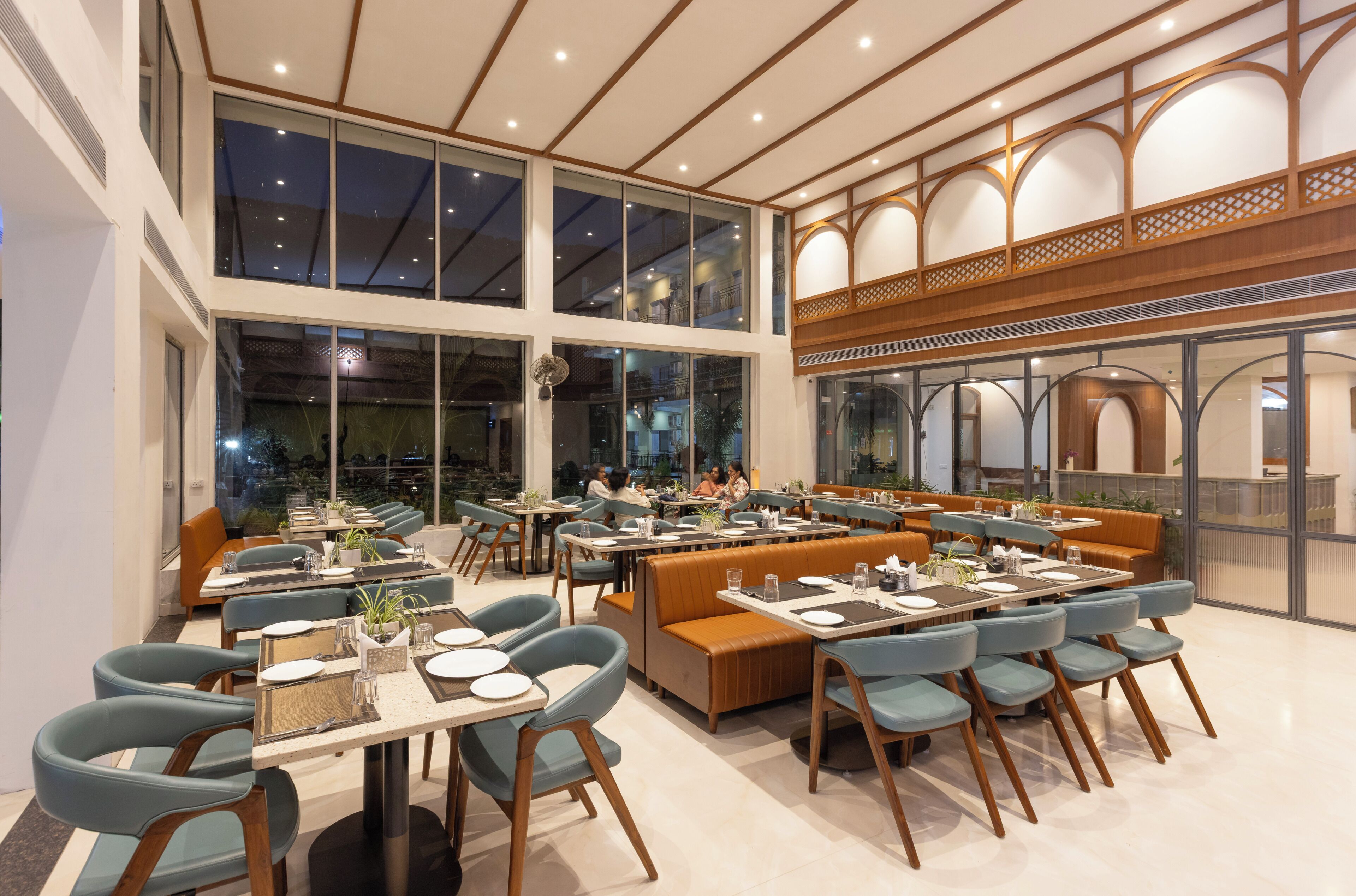 Un restaurante con varias áreas de comedor, incluyendo cabinas y mesas, grandes ventanales y un techo alto.