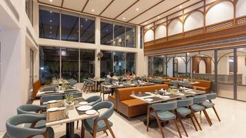 Un restaurante con varias áreas de comedor, incluyendo cabinas y mesas, grandes ventanales y un techo alto.