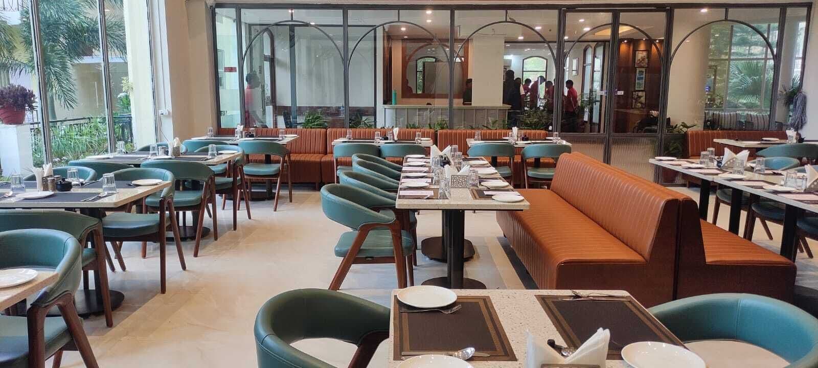 Un restaurante con mesas preparadas, platos y cubiertos, y un amplio ventanal con vistas a la calle.
