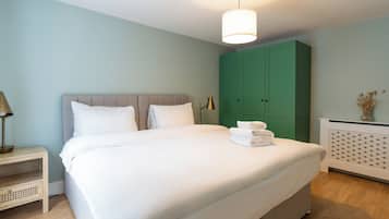 A neatly made bed with white linens, a bedside table with a lamp, and a green wardrobe in a room with light blue walls.