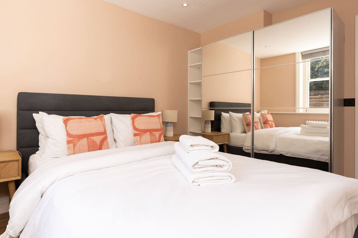 A hotel room with a bed, a nightstand, a lamp, and a large mirror.