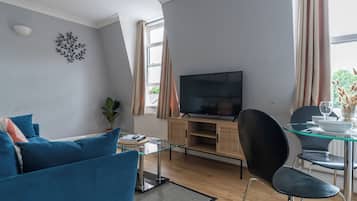 A modern living room with a flat-screen TV, blue sofa, glass dining table, and a potted plant.