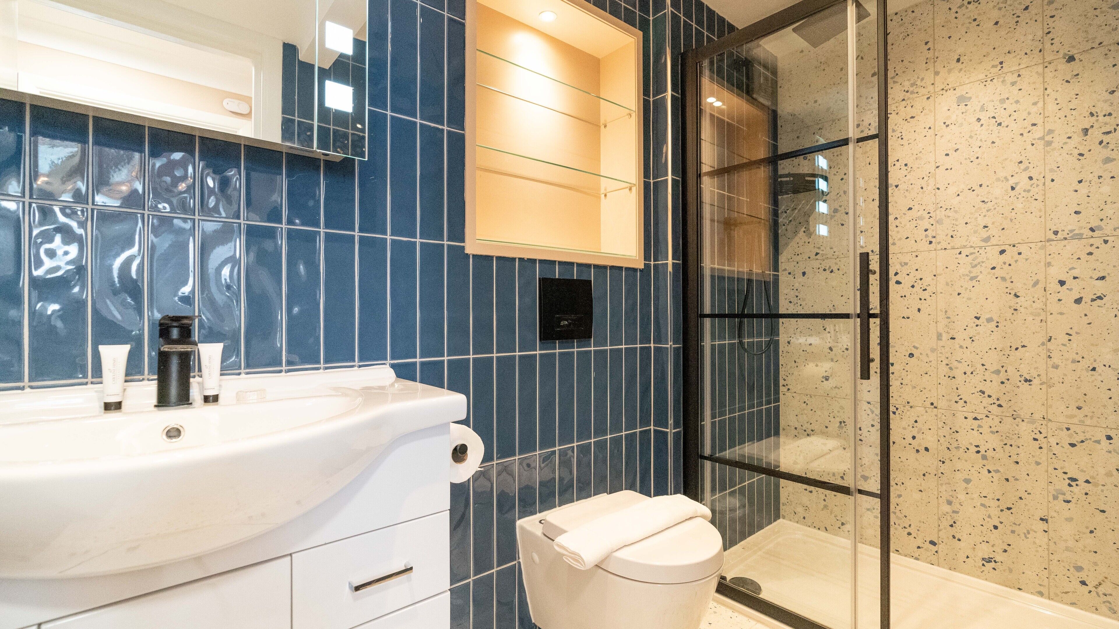 Une salle de bain moderne avec un lavabo blanc, un miroir et une cabine de douche en verre.