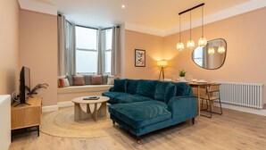 Un salon moderne avec un canapé de couleur turquoise, une table basse en bois et un coin repas comprenant une petite table et des chaises.
